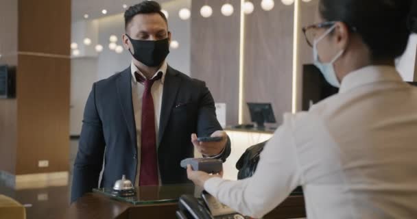 Młody Przedsiębiorca Noszący Medyczną Maskę Twarz Płaci Usługi Hotelowe Smartfonem — Wideo stockowe