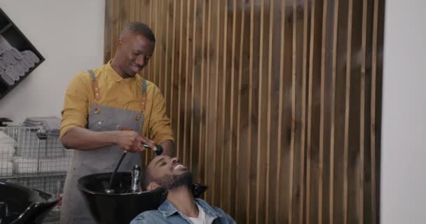理发师给顾客洗头 而放松的年轻人则在理发店里享受着微笑的待遇 卫生和健康温泉沙龙概念 — 图库视频影像