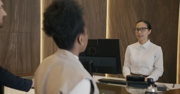 酒店接待员友好的年轻女性正在和客人们交谈 并在大堂里给客人们颁发重要的名片 通信和通信概念 — 图库视频影像