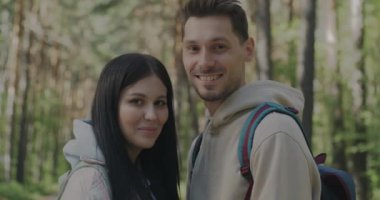 Sırt çantalarında kameraya bakıp gülümseyen yeşil ormanda duran mutlu genç bir çiftin portresi. Turizm ve ilişki kavramı.