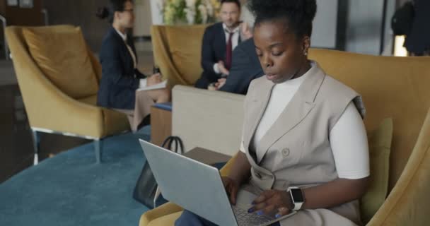 成功的非洲裔美国女商人正在酒店大堂与笔记本电脑合作 他们的工作集中在忙于网络建设的在线活动 — 图库视频影像