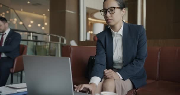 迷人的中东女商人在酒店大堂与笔记本电脑打交道 而穿着西服的人则在后台行走 现代技术和通勤概念 — 图库视频影像
