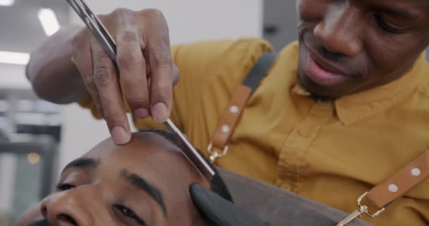 仔细理发的理发师在理发店里用锋利的剃须刀剃光非洲裔美国人的胡子 同时满足顾客享受良好服务的要求 — 图库视频影像