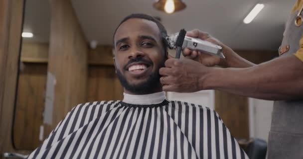 Portrét Veselého Afroameričana Usmívajícího Kameru Zatímco Holič Holí Vlasy Elektrickým — Stock video