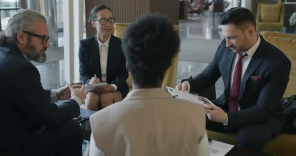 多国籍ビジネスチームの男性と女性は ホテルのロビーでの会議中にアイデアを共有しています コミュニケーションとパートナーシップの概念 — ストック動画
