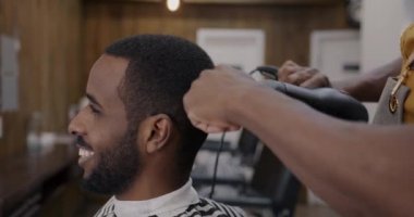 Berber dükkanında saçını elektrikli kurutma makinesiyle fırçalarken gülümseyen neşeli bir müşteri. Modern alet ve güzellik salonu konsepti.