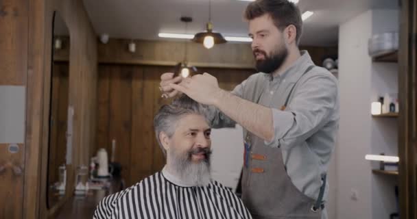 理发师穿着围裙裁剪男人的头发 与客户一起工作 并在理发店里微笑 美容美发和专业美发师概念 — 图库视频影像