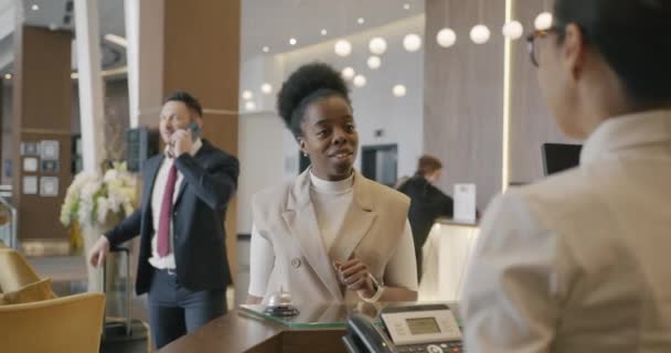 現代のホテルのフロントでは 多民族の起業家が鍵となるカードを入手しており 管理者と宿泊について話し合っている — ストック動画
