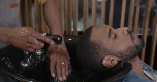 Zbliżenie Młodego Afroamerykanina Uśmiechającego Się Podczas Fryzjera Myjącego Włosy Umywalce — Wideo stockowe