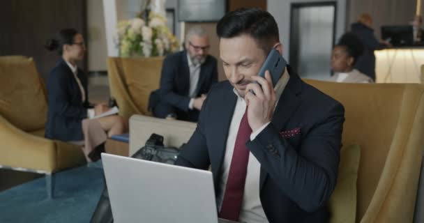 成功的企业家穿着西服与笔记本电脑一起工作 并在酒店休息室用手机交谈 商业和现代技术概念 — 图库视频影像