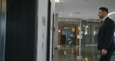 Modern otel lobisinde asansör bekleyen başarılı genç işadamının yan görüntüsü düğmeye basıyor ve tek başına duruyor. İnsanlar ve iç konsept.