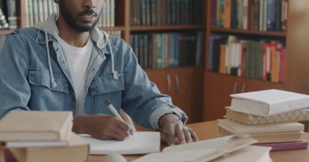 アフリカ系アメリカ人の男性が図書館で本を勉強しているノートに情報を書いて知識を得る 教育と文学の概念 — ストック動画