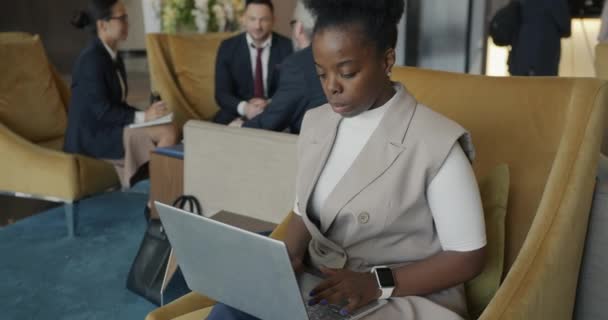 野心的なアフリカ系アメリカ人のビジネスマンは ホテルのラウンジに座ってノートパソコンのタイピングで働いています ビジネスと現代のデバイスの概念 — ストック動画