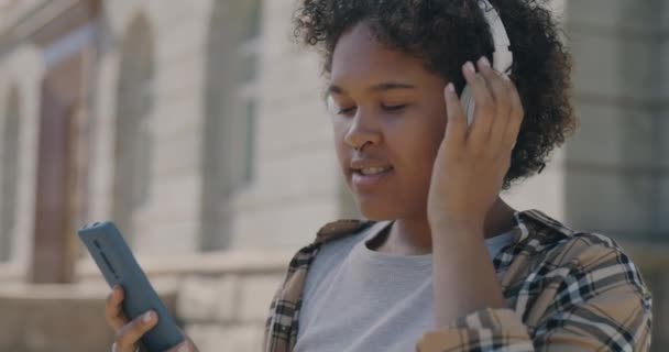 거리에서 헤드폰 스마트폰을 사용하여 음악을 아프리카 미국인 소녀의 움직임 방식의 — 비디오