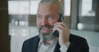 Yetişkin bir iş adamının portresi cep telefonuyla konuşuyor ve otel lobisinde dikilip gülüyor ve modern cihazlar kullanıyor. İletişim ve insan kavramı.