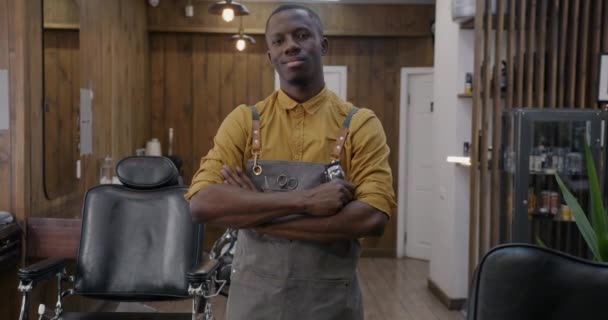 幸せなアフリカ系アメリカ人男性理容師のスローモーションポートレート腕を交差し カメラを見て理容室で職場に立っている 仕事と美容室のコンセプト — ストック動画