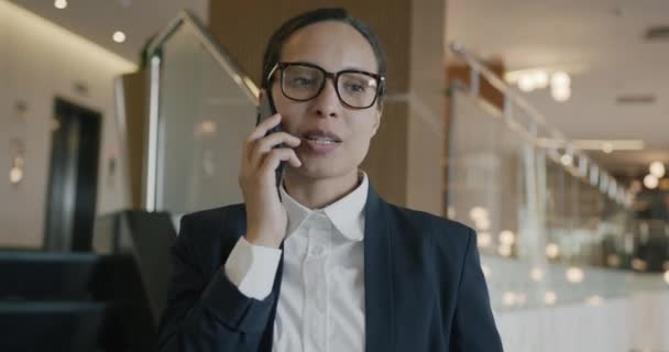 エレガントな服やメガネを着用してホテルのロビーから携帯電話で話す成功した出産ビジネスの女性の肖像画 コミュニケーションと人々の概念 — ストック動画