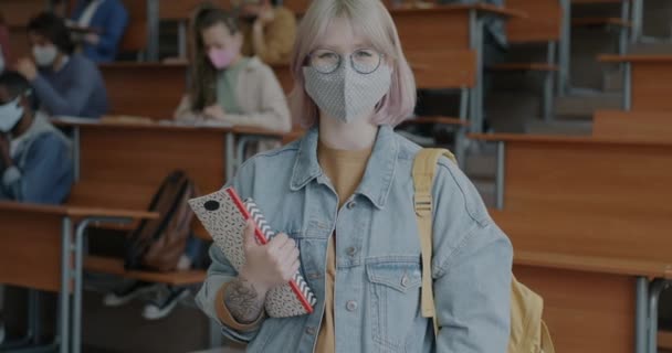 大学で医学マスクを身に着けている女性学生のスローモーションの肖像画は Covid 19危機の間に本を保持 人々とパンデミックの制限の概念 — ストック動画