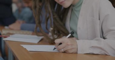 Kadın öğrenci bir grup insanla masa başında otururken elinizi kalem sınavına sokun. Bilgi ve üniversite eğitimi kavramı.