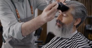 Berber berber dükkanında müşteriler gülümserken erkeklerin saçlarını yüzlerinden ayıklıyor. Gri saçlı adam stüdyoda güzellik rutininin keyfini çıkarıyor..