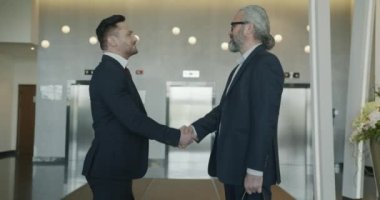 Takım elbiseli neşeli iş adamları modern otel lobisinde el sıkışıyorlar. Halk ve girişimcilik kavramı.