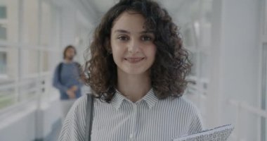 Üniversite lobisinde durup eğitimin tadını çıkaran genç bir kızın ağır çekimde portresi. Pozitif duygu ve gerçek insanlar kavramı.