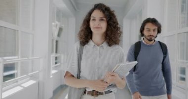 Lise koridorunda yürüyen ve elinde kitaplarla el sallayan genç kız öğrencinin yavaş çekimde portresi. Gençlik ve modern eğitim kavramı.