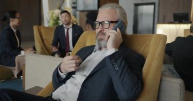 Takım elbiseli olgun bir adamın portresi cep telefonuyla konuşuyor iş konuşuyor ve otel lobisinde gülümsüyor. İş yeri ve iletişim konsepti.