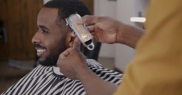 床屋でシェービングマシンで髪を削除しながら アフリカ系アメリカ人の男笑顔の側面図 美容室設備と人のコンセプト — ストック動画