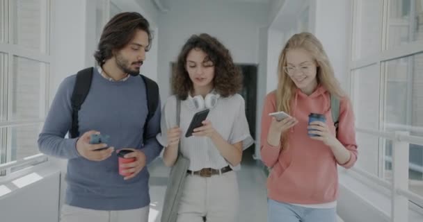 大学の廊下を歩き ソーシャルメディアのコンテンツを議論するスマートフォンを使用して楽しい若者のスローモーションの肖像画 教育と近代技術の概念 — ストック動画