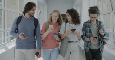 Çeşitli öğrenci grupları üniversite koridorlarında yürüyüp, akıllı telefon içeriğinin tadını çıkarırken birlikte gülüp eğleniyorlar. İnsanlar ve iletişim konsepti.
