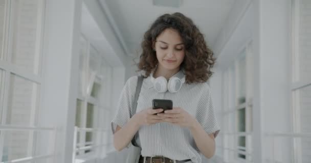 Dolly Nin Üniversite Koridorunda Akıllı Telefon Mesajlarıyla Yürüyen Mutlu Genç — Stok video