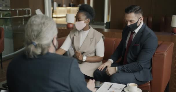 医療マスクを身に着けている若いアフリカ系アメリカ人女性は その後 同僚と話す消毒剤で手を噴霧ホテルでビジネスミーティングに来ています — ストック動画
