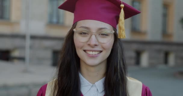 成功的女大学生穿着长袍戴帽子站在校园里的画像 教育和雄心勃勃的青年概念 — 图库视频影像