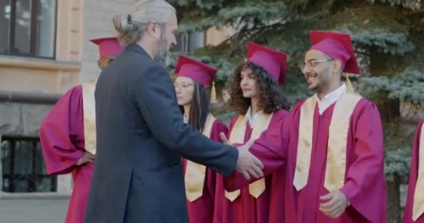 在毕业典礼上 成熟的大学校长与学生握手 拥抱年轻人 向他们表示祝贺 教育和成绩概念 — 图库视频影像