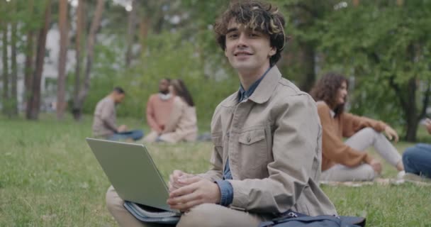 Медленный Портрет Веселого Молодого Человека Сидящего Траве Парке Ноутбуком Улыбающегося — стоковое видео