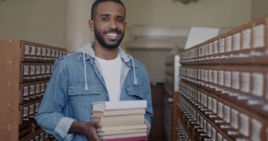 Üniversite eğitiminin keyfini çıkarırken gülümseyen kitaplarla kütüphanede duran zeki, Afro-Amerikan bir adam. Bilgi ve okuryazarlık kavramı.
