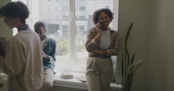 アフリカ系アメリカ人の学生が携帯電話で話し 大学のロビーでタブレットを使用しています 現代の技術と若者の概念 — ストック動画