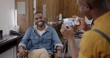 Berber, akıllı telefon kamerasıyla müşterinin fotoğrafını çekerken Afro-Amerikan bir adam berber dükkanında eğleniyormuş gibi poz veriyor. Fotoğraf ve güzellik salonu konsepti.