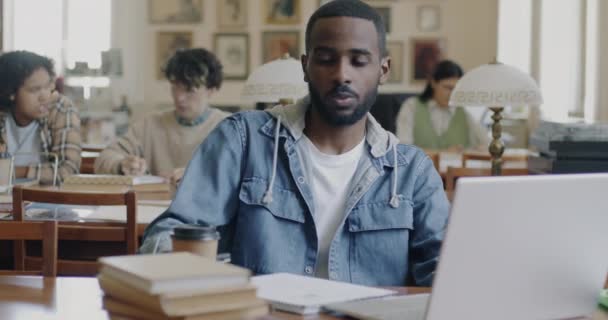 Estudiante Universitario Afroamericano Trabajando Con Portátil Bebiendo Sacar Café Biblioteca — Vídeo de stock