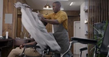 Berber dükkanında saç kesimine hazırlanırken önlük giyip peleriniyle gülen neşeli bir berber. Kuaför salonu ve müşteri tedavi konsepti.