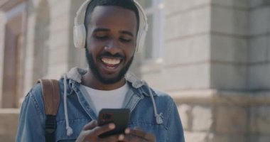 Afrika kökenli Amerikalı bir adam şarkı söyleyip dans ediyor kulaklıkla müzik dinliyor ve güneşli bir yaz gününde şehirde akıllı telefon kullanıyor. Boş zaman ve şehir yaşam tarzı konsepti.