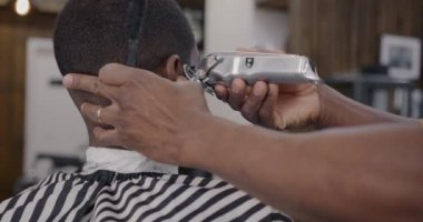 Afro-Amerikalı berber müşterisinin tıraş makinesiyle kuaför tarafından tedavi edilişinin arkası. Ekipman ve güzellik konsepti.