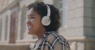 Şehirde dans eden, kulaklıkla müzik dinleyen Afro-Amerikan kadının yavaş çekim portresi. Gençlik ve kentsel yaşam tarzı kavramı.