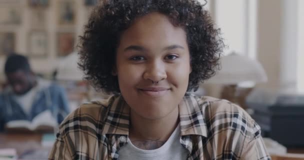 アフリカ系アメリカ人の少女が 高校図書館で勉強しながら屋内で笑っている姿が描かれています 若者と教育の概念 — ストック動画