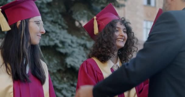 身穿西服 头戴毕业帽的成熟男子在校园里拥抱学生 并在户外恭贺年轻人 教育和成功概念 — 图库视频影像