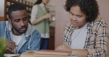 Afrika kökenli Amerikalı öğrenciler lise ödevlerini birlikte yapıyor kitap okuyor ve kütüphanede yazı yazıyorlar. Eğitim ve edebiyat kavramı.