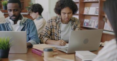 Kütüphanede çalışan çeşitli öğrenci grupları dizüstü bilgisayar ve akıllı telefon kullanarak kitap okuyor. Afro-Amerikalı bir kadın iyi haberlerle, gülümseyen bir heyecanla mesaj alıyor.