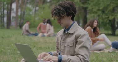 Parkta çalışan zeki bir genç, online eğitime odaklanmış dizüstü bilgisayar kullanıyor. Z jenerasyonu ve modern teknoloji kavramı.