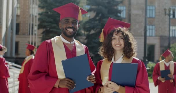非洲裔美国男性和白人女性毕业生穿着砂浆板站在校园里的肖像 人与高等教育概念 — 图库视频影像